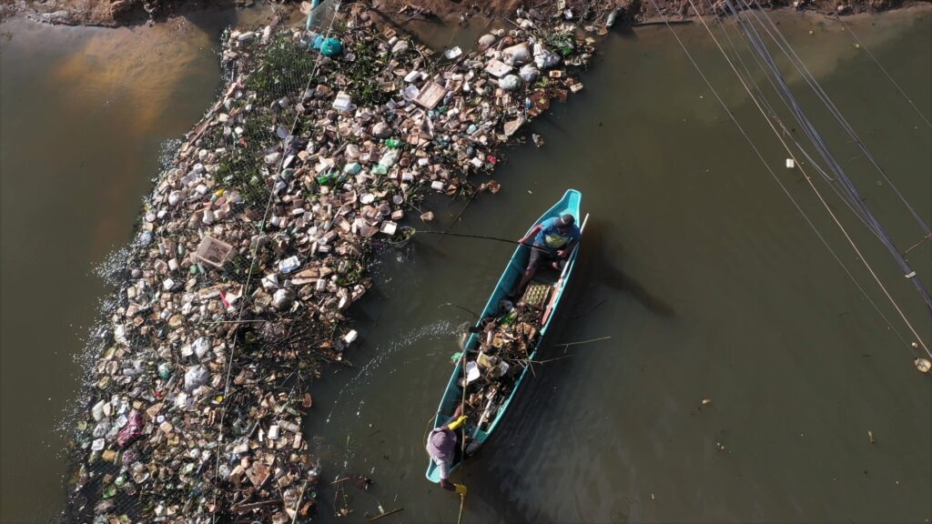 Aerial view of a man in a small boat beside a floating mass of plastic waste