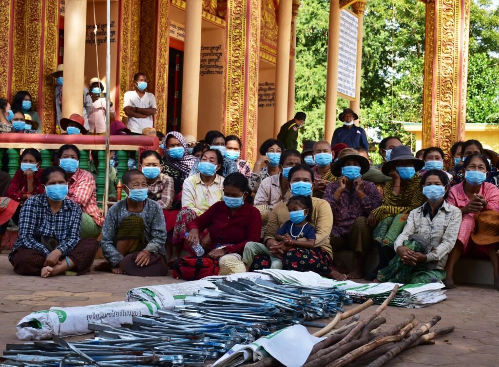 Villagers in face masks sit together at a community meeting in a pagoda hall
