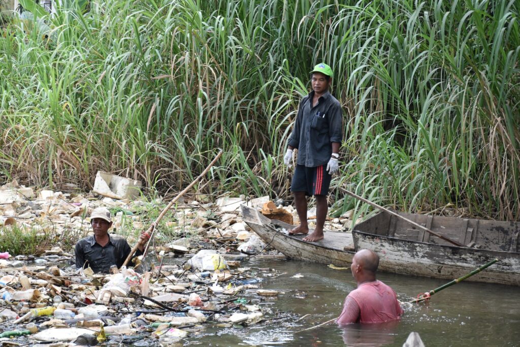 A man wades through floating plastic beside a boat