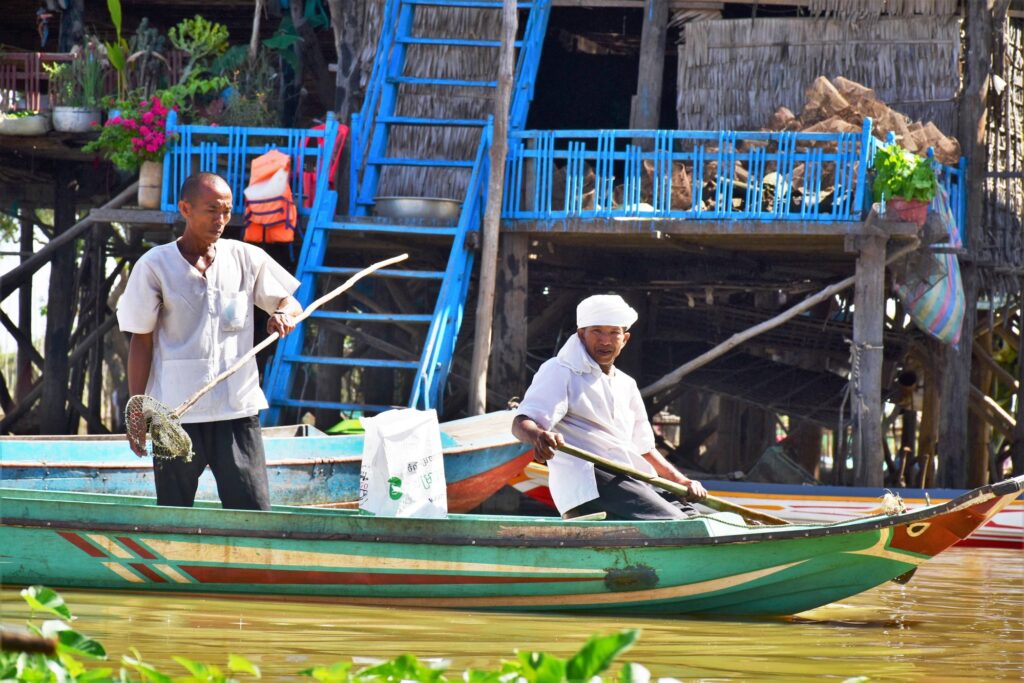 Two men in a boat collect a bag of plastic beside a stilt house