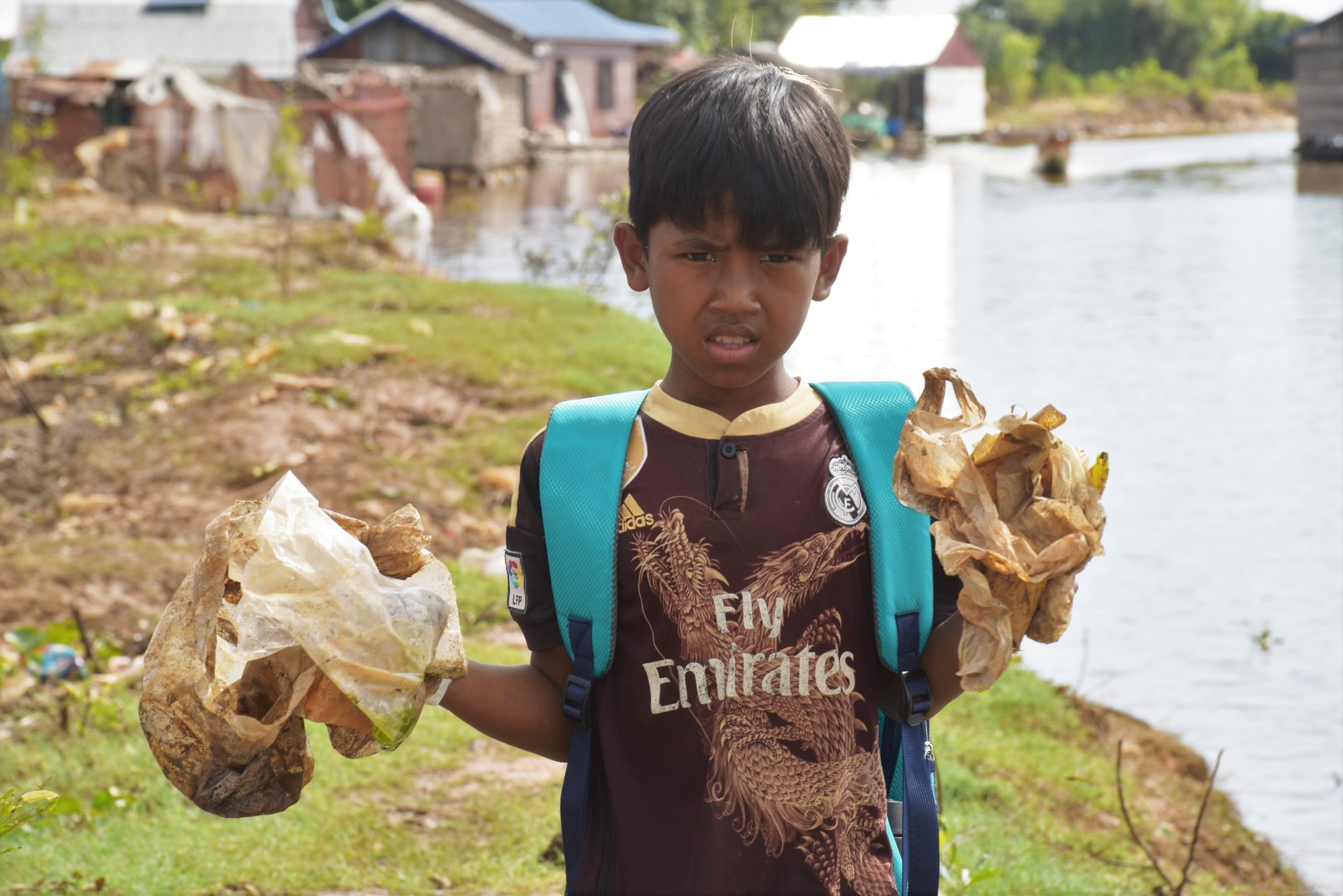 A boy holds up plastic bags he collected by the water