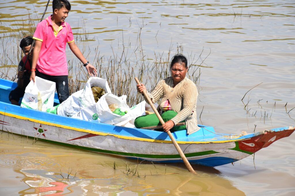 A woman paddles a boat loaded with bags of collected plastic