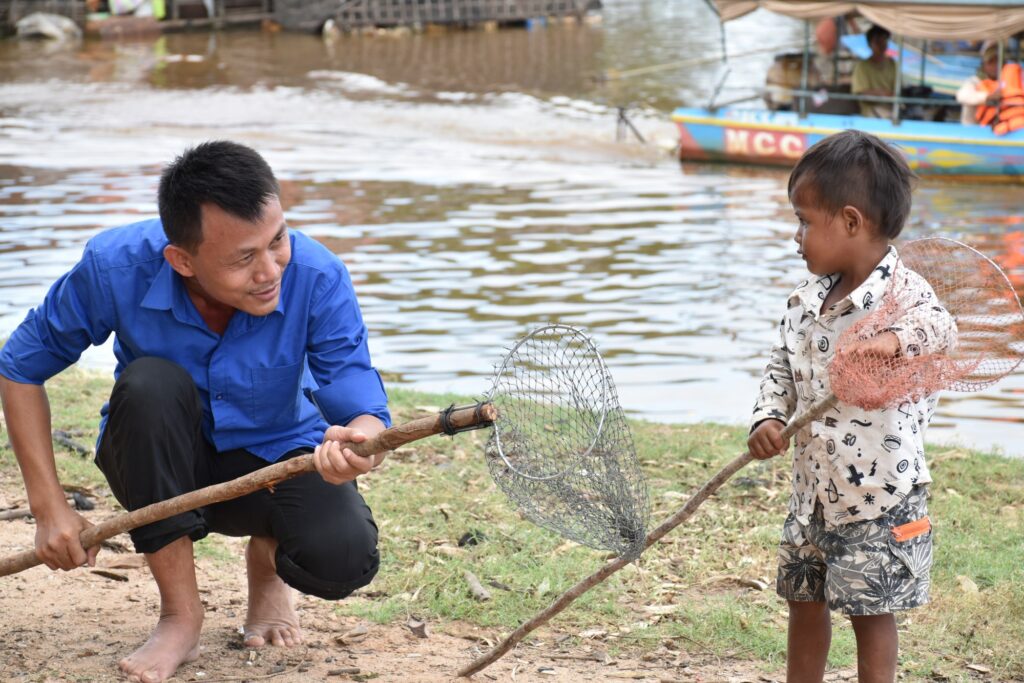 A man and a boy collect plastic with long nets at the water's edge
