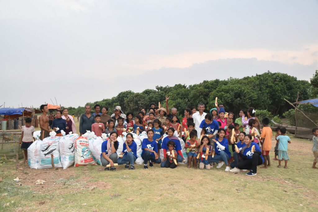 A large group poses with bags of collected plastic on the shore