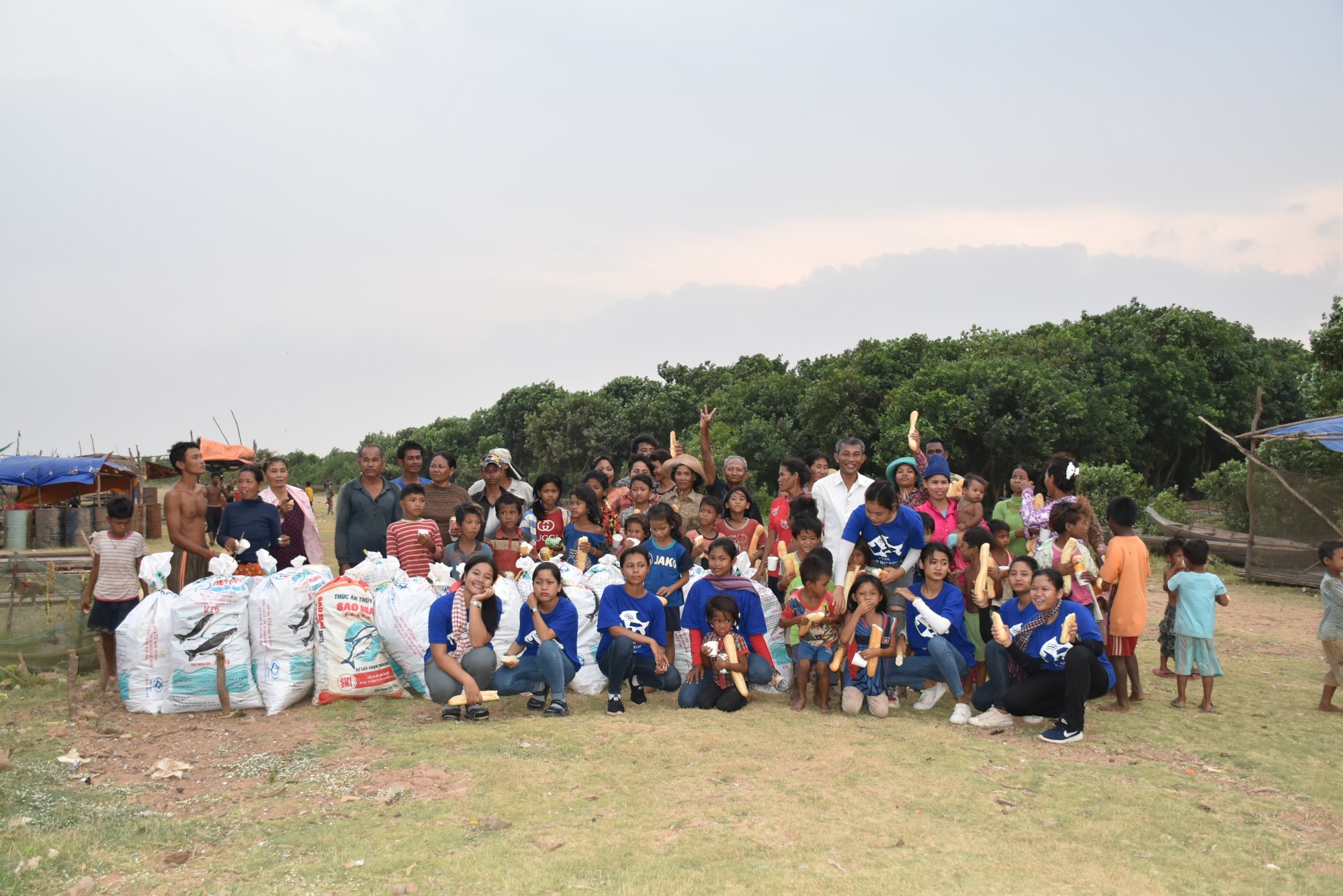 A large group poses with bags of collected plastic on the shore