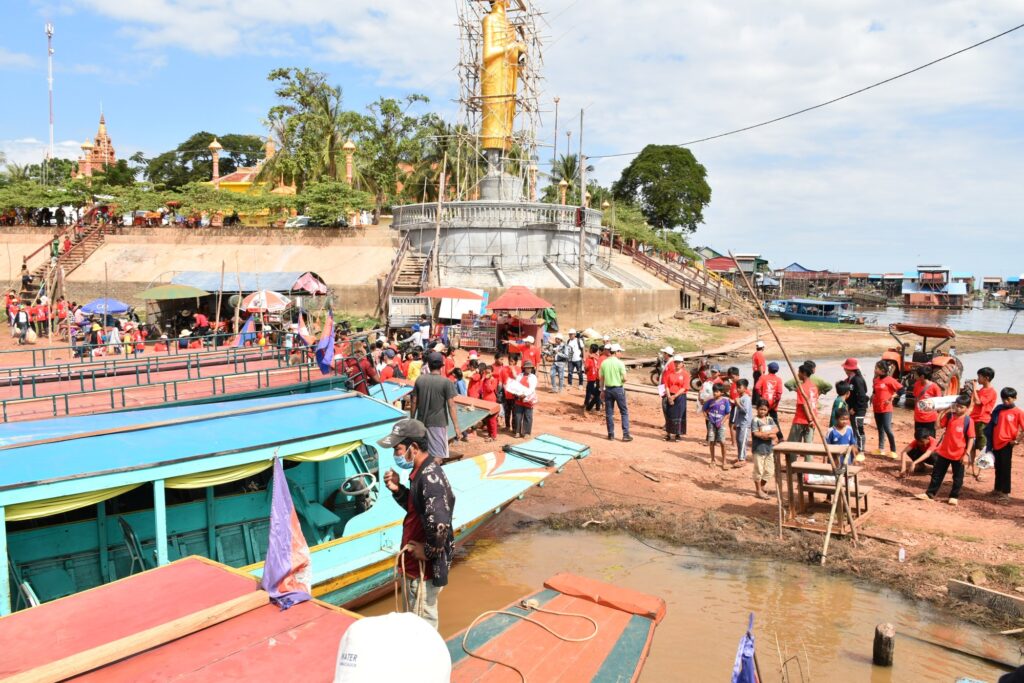 Volunteers in red shirts gather on the shore beside moored boats