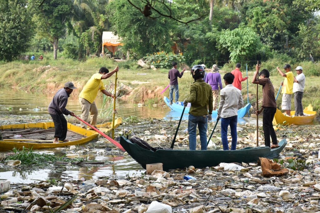 Villagers use poles and boats to clear plastic from the water's edge