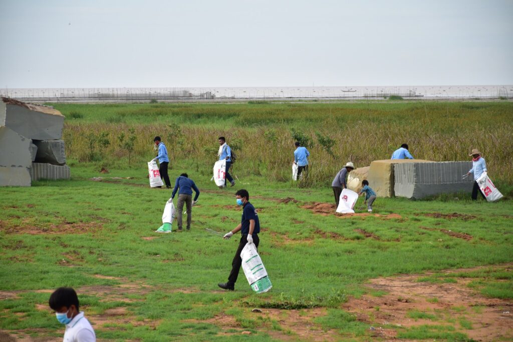 Volunteers with bags collect plastic across a grassy field